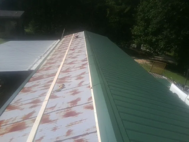 Old rusted panels beside newly installed green metal roofing — Wind Damage Roof Repair by Roofing Brothers in Ridge