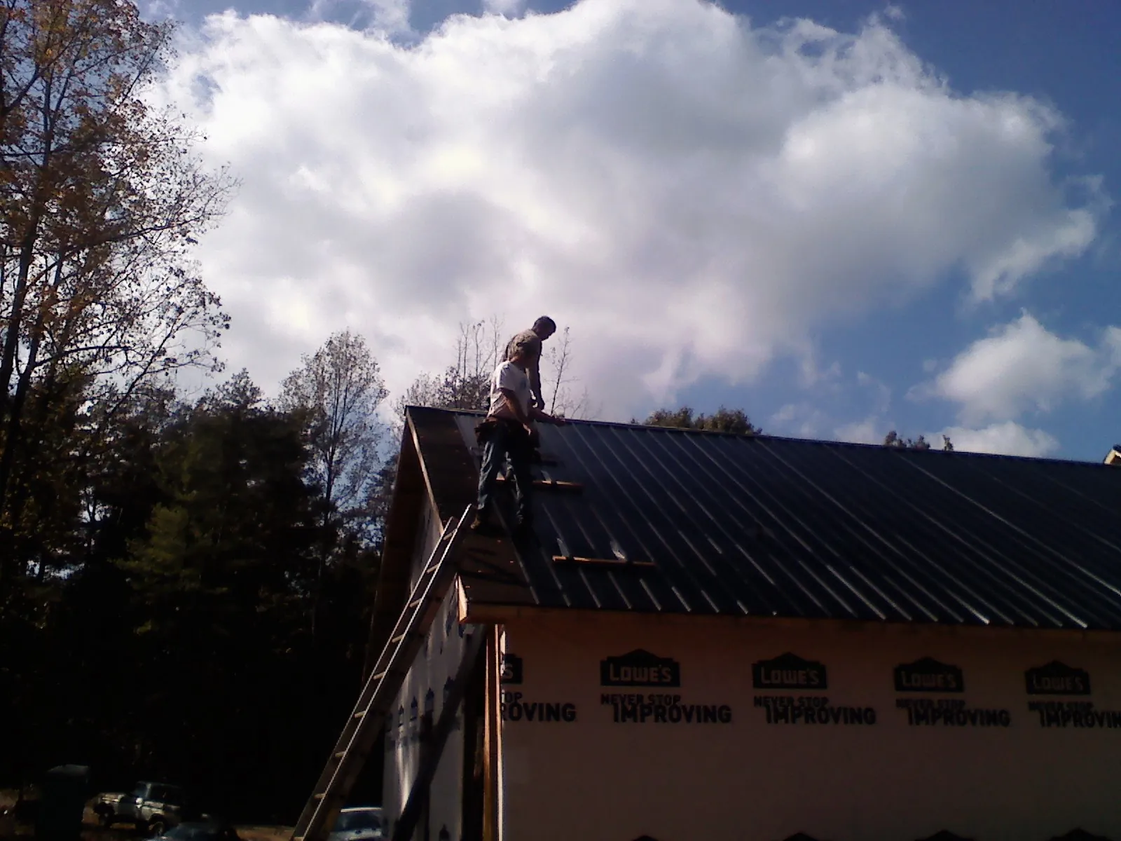 Roofer fastening dark metal panels high against a cloudy sky, from a Roof Inspection job in Ridge